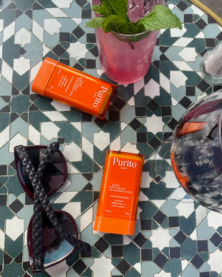 Purito seoul sun stick oranje op een terras tafel met drankjes - glow skin products